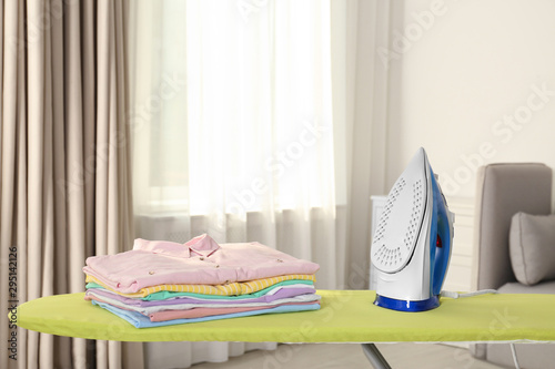 Board with modern iron and clean laundry at home photo