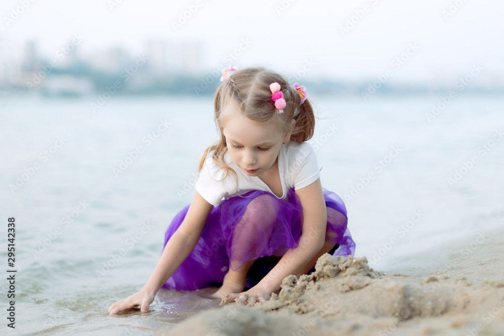 Happy child playing with sand at the beach in summer