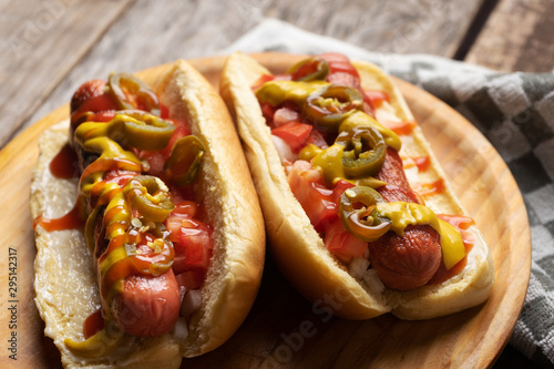 Slika na platnu Hot dog with jalapeno pepper and tomato on wooden background