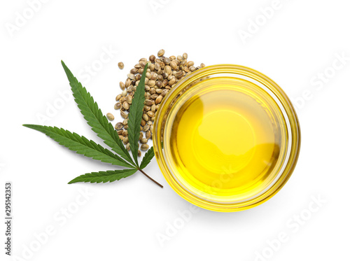 Bowl with hemp oil, leaf and seeds on white background, top view photo