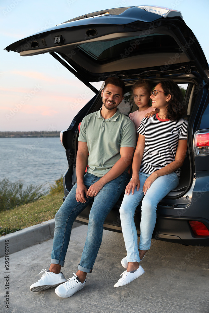 Happy young family sitting in car trunk on riverside Happy young family sitting in car trunk on riverside