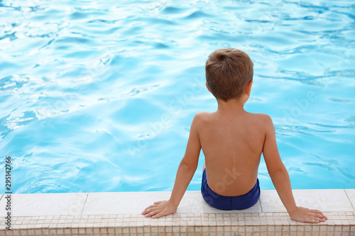 Cute little boy sitting near outdoor swimming pool