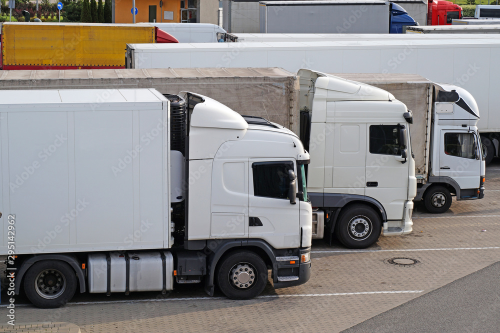 Various types of trucks in the parking lot next to the motorway.