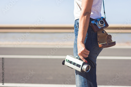 Filmmaker waiting standing together with her old film cameras next to a road