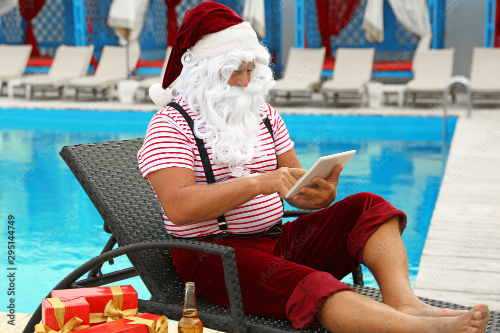 Fototapeta premium Authentic Santa Claus with tablet resting on lounge chair at resort