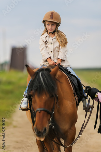 Little girl in equestrian helmet riding a horse.