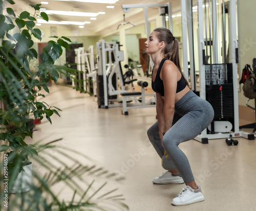Young fitness woman doing squats exercise with kettlebell in the gym. Functional training with free weights © splitov27