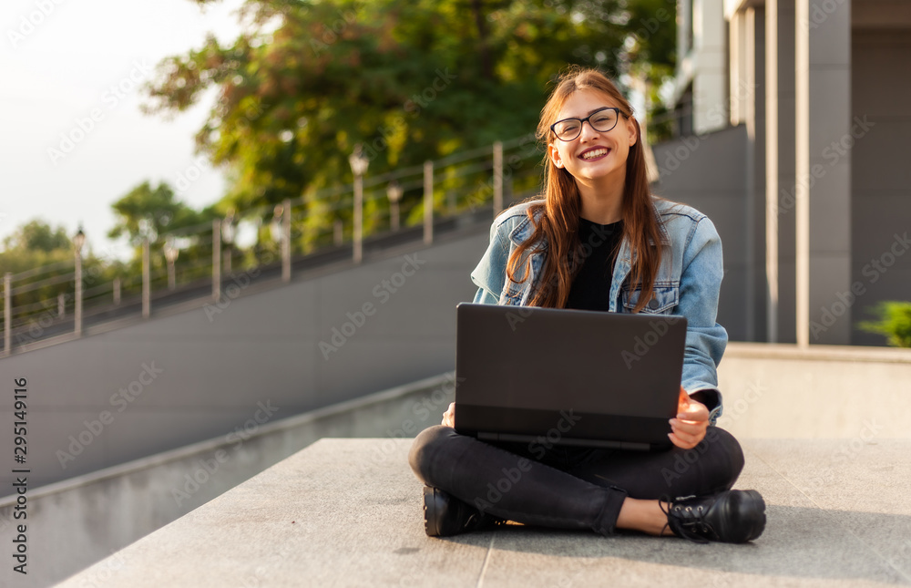 Young modern woman student in a denim jacket sitting on the stairs with laptop. Distance learning. Modern youth concept. Young modern woman student in a denim jacket sitting on the stairs with laptop. Distance learning. Modern youth concept.