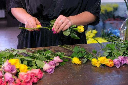 Floral business concept. Professional florist woman prepares flowers to bunch bouquet. She cuts rose thorns in shop, closeup hands. Working day in floristic studo store salon. photo