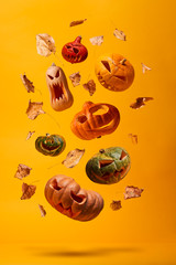 Several halloween pumpkins and dry leaves on empty orange background