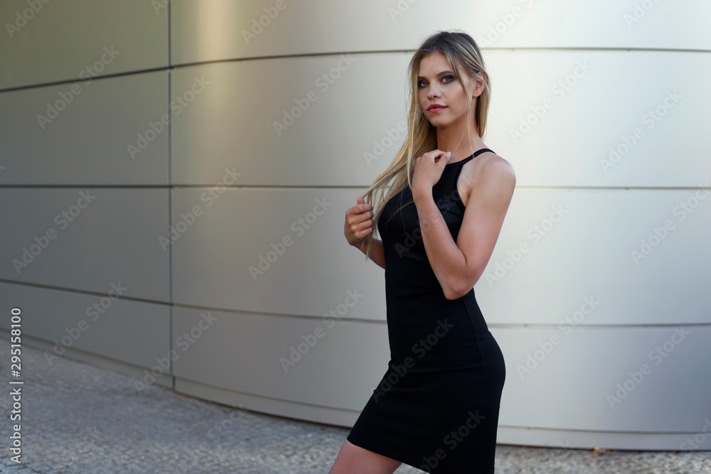 Female model posing in classic black dress. Wall of modern building in the background. Female model posing in classic black dress. Wall of modern building in the background.
