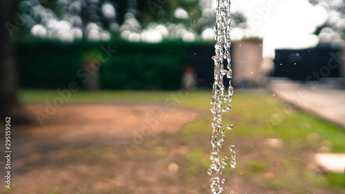 Stream of crystal clear water pouring from iron tap on garden background. Flow of water, transparent bubbles