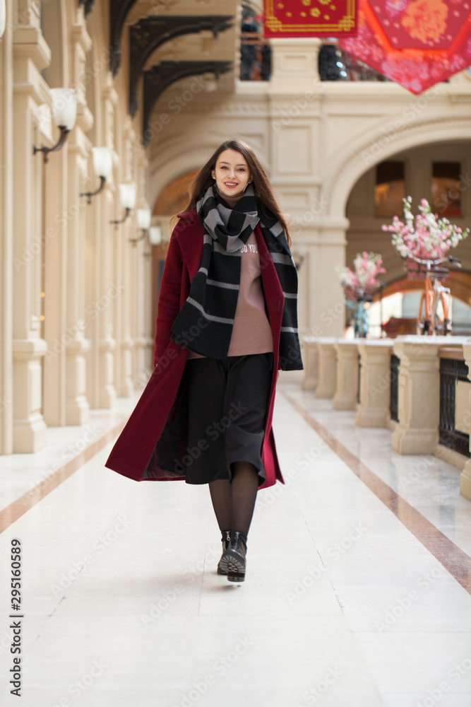 Beautiful girl in stylish in a long burgundy coat, indoor shop Beautiful girl in stylish in a long burgundy coat, indoor shop