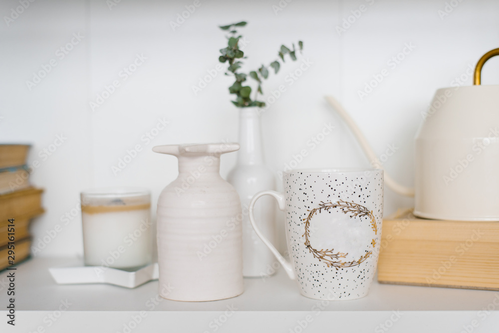 Mug, vase and candle on the shelf in the living room in white and beige colors