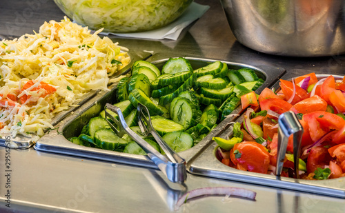 ingredients at a falafel bar with metal vegetable tongs cabbage cucumber tomatoes