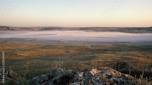 Dry grass grown on large rocks sways in a strong wind at sunset against a background of pink lake, open spaces with dry yellow grass and low mountains in summer. photo