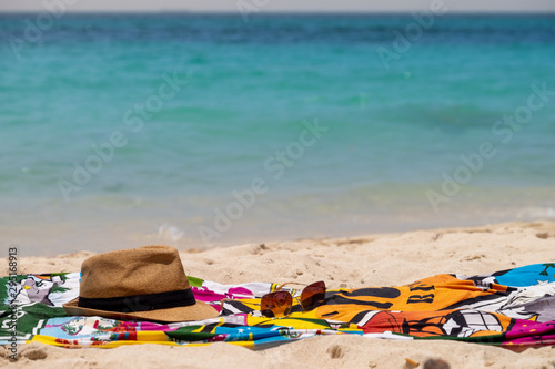 Fototapeta Naklejka Na Ścianę i Meble -  Pareo de playa , sombrero y gafas en una playa desierta junto al mar en el atardecer.