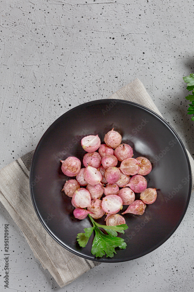 Beautiful roasted radishes in a black plate on concrete table, close up.