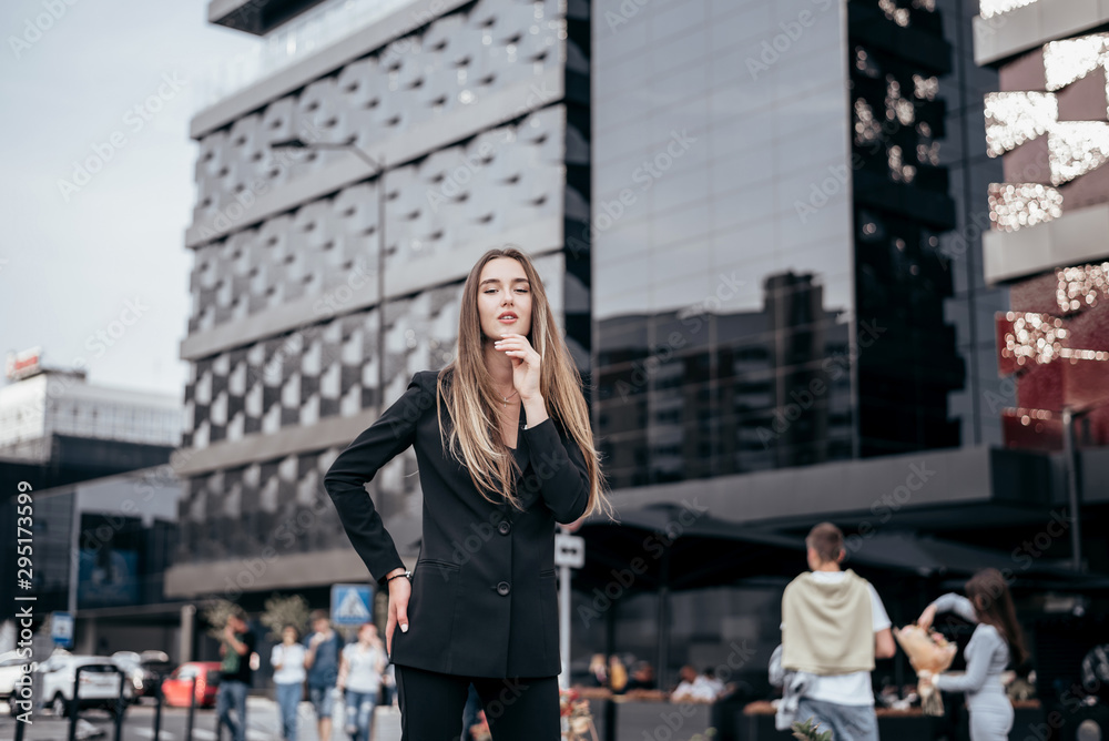 Young and attractive business girl on the background of the city in a beautiful black suit.