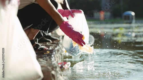 Low angle view of ecology volunteers picking up plastic trash and cleaning polluted lake in parkland. Young friendly people supporting environment conservation. Recycling concept.