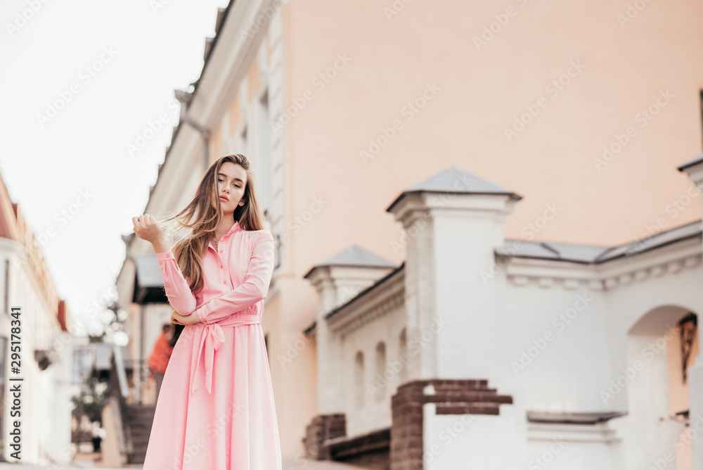 Fototapeta premium A young, beautiful girl in a pink dress walks through the beautiful streets in the city. Very beautiful portraits of a girl in the city.