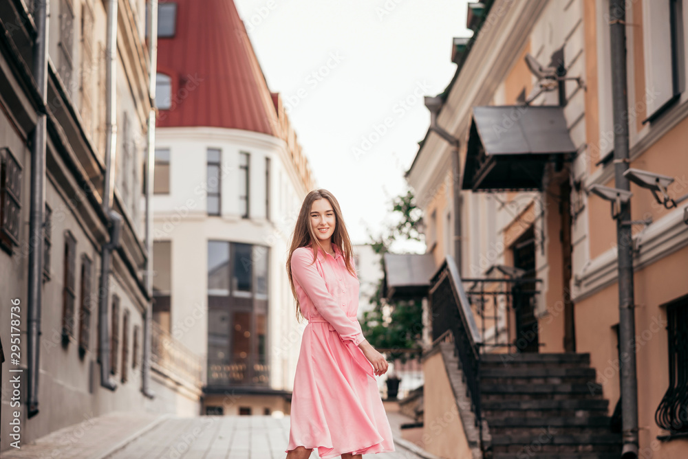 A young, beautiful girl in a pink dress walks through the beautiful streets in the city. Very beautiful portraits of a girl in the city.