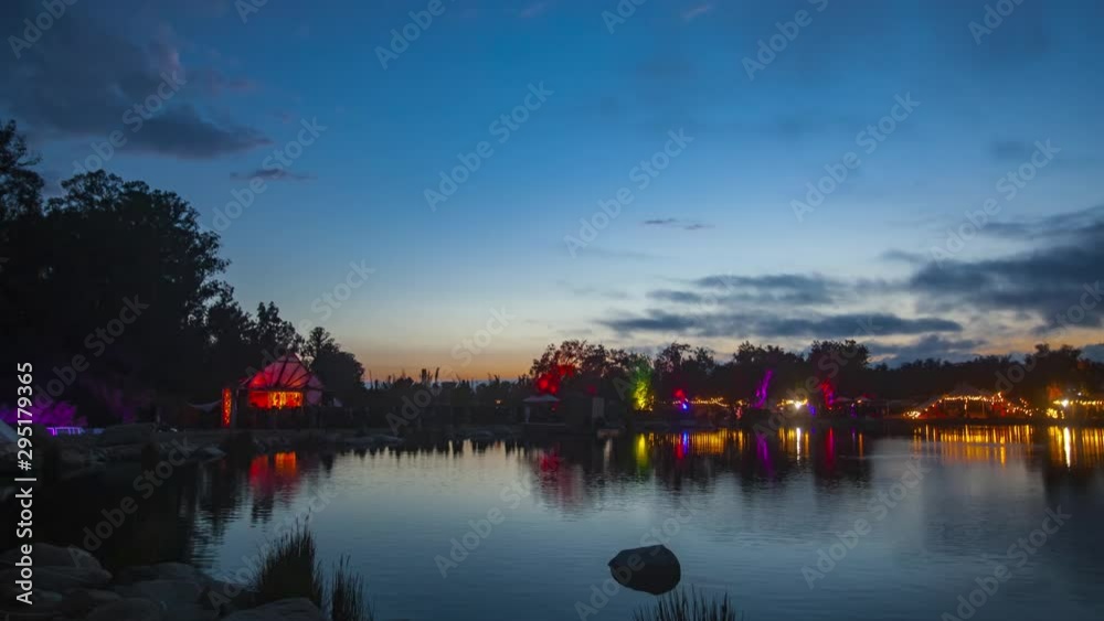 Timelapse of outdoors music festival going from day into night with lights and tents in front of a lake. Timelapse of outdoors music festival going from day into night with lights and tents in front of a lake.