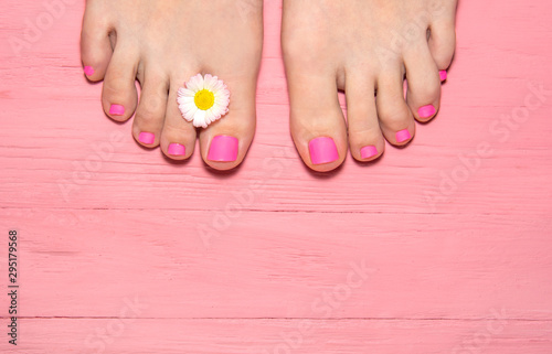 hot pink pedicure. top view of legs with pedicure. leg against the background of a pink plank with a flower frame between the fingers. pink wood background