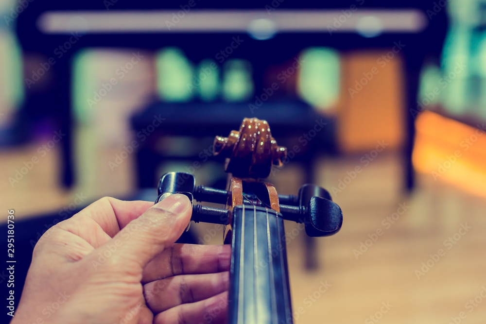 Hand tuning violin with blurry piano in music room or stage. music instrument concept. Hand tuning violin with blurry piano in music room or stage. music instrument concept.