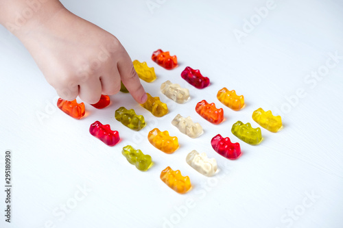 Children's vitamins in the form of bears are arranged in rows.  A lot of multi-colored jelly sweets for children.  The hand of the child reaches and takes a vitamin or candy