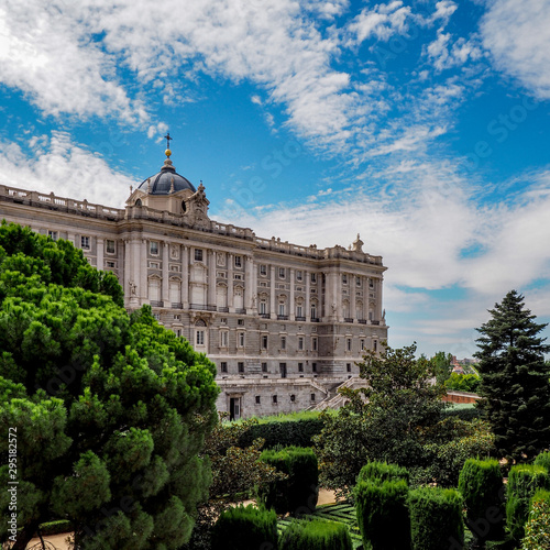 Side view of the Royal Palace of Madrid with green garden foreground and blue sky