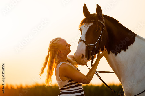 Frau schaut im Sonnenuntergang ihr Pferd verliebt an