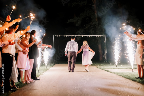 A crowd of young happy people with sparklers in their hands during celebration. Sparkler in hands on a wedding - bride, groom and guests holding lights in hand. Sparkling lights of bengal fires.