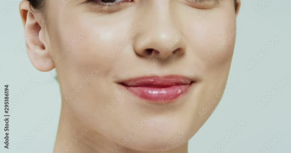 Close up of the bottom part of the female face, mouth rose lip gloss of the Caucasian woman, then camera moving to the eyes and full portrait on the white wall background. Close up of the bottom part of the female face, mouth rose lip gloss of the Caucasian woman, then camera moving to the eyes and full portrait on the white wall background.