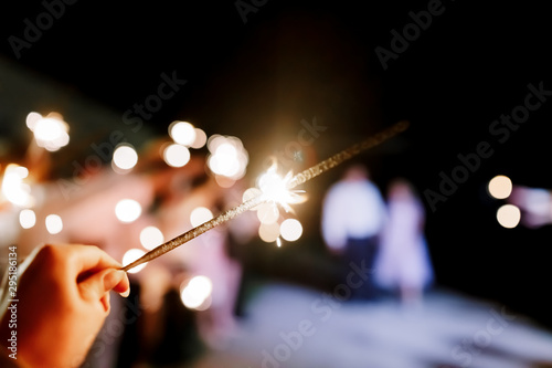 A crowd of young happy people with sparklers in their hands during celebration. Sparkler in hands on a wedding - bride, groom and guests holding lights in hand. Sparkling lights of bengal fires.