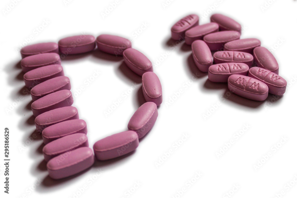 Pink oval tablets in a shape of letter D next to pile of same pills. Isolated on white background. Pink oval tablets in a shape of letter D next to pile of same pills. Isolated on white background.