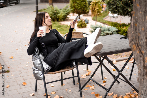 girl in black clothes and white sneakers drinking coffee and talking on the phone