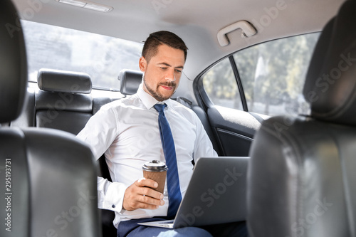 Successful businessman with laptop drinking coffee in modern car © Pixel-Shot
