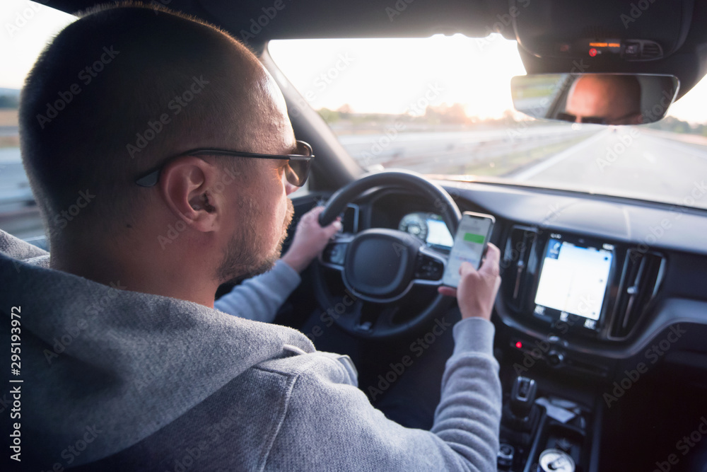 Man driving car using mobile phone texting message or calling..Driver holding smart phone while driving car on the road..People transportation dangerous lifestyle concept. Man driving car using mobile phone texting message or calling..Driver holding smart phone while driving car on the road..People transportation dangerous lifestyle concept.