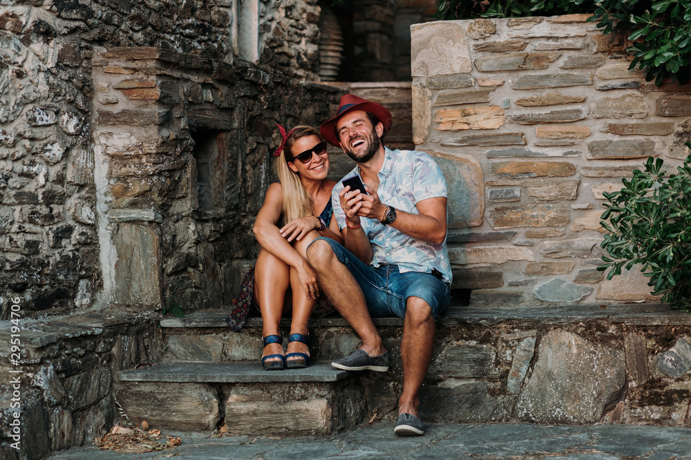 Young couple using smartphone on the stairs of an old town in Greece