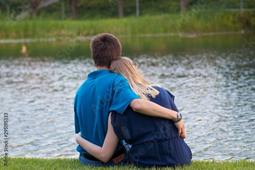 Young couple sitting and holding each other beside a small pond at evening