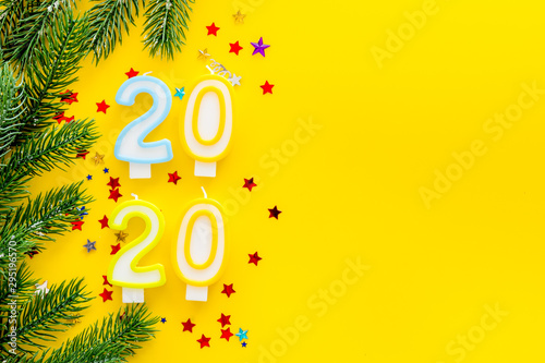 2020 New Year design. Date laid out by candles near fir branches on yellow background top view frame copy space