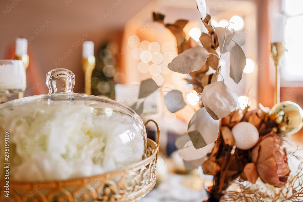 New Year mood, Christmas tree. Rectangular table covered with a gold tablecloth, decorated with candles and a vase of flowers with flowers for celebration. Table with a gold tablecloth.