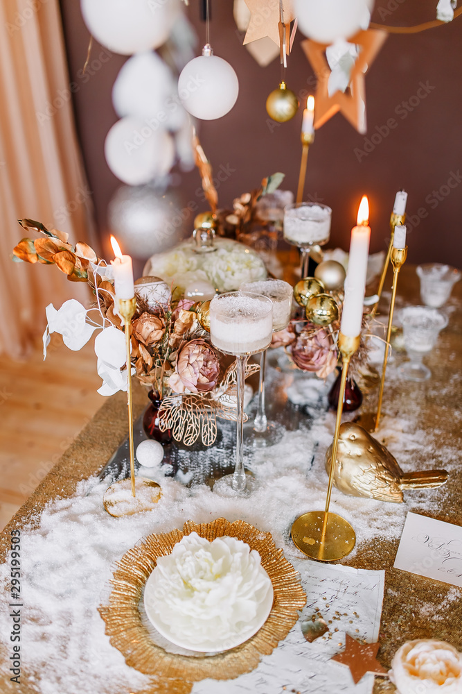 New Year mood. Table with a gold tablecloth, decorated with candles for celebration. Festive still life by candlelight. Graphics of beautiful calligraphy with a flower on a plate.