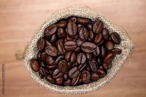 Close up, brown coffee beans in a cloth bag on an old wooden background. Top view.