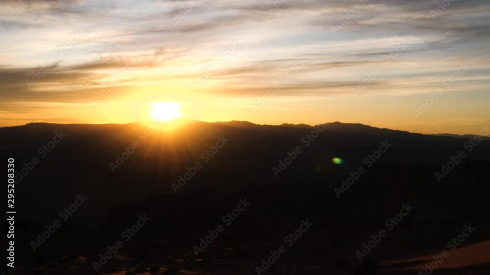 Time Lapse-Sun goes down behind distant desert hills casting a golden glow on brightly lit clouds. Foreground hills in dark silhouette. Time Lapse-Sun goes down behind distant desert hills casting a golden glow on brightly lit clouds. Foreground hills in dark silhouette.