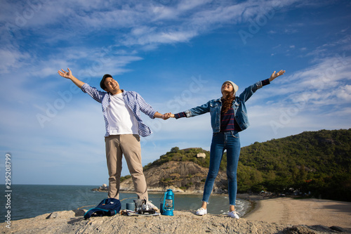 Asian couple in blue shirt with coffee cup and vintage camera picnic on the mountain near the beach sea view happy and smile face
