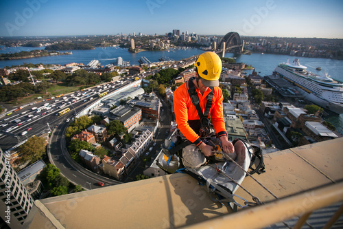 Rope access worker wearing yellow hard hat, long sleeve shirt, Full safety body harness, working at height, and abseiling off from the high rise building near circular quay, Sydney, Australia