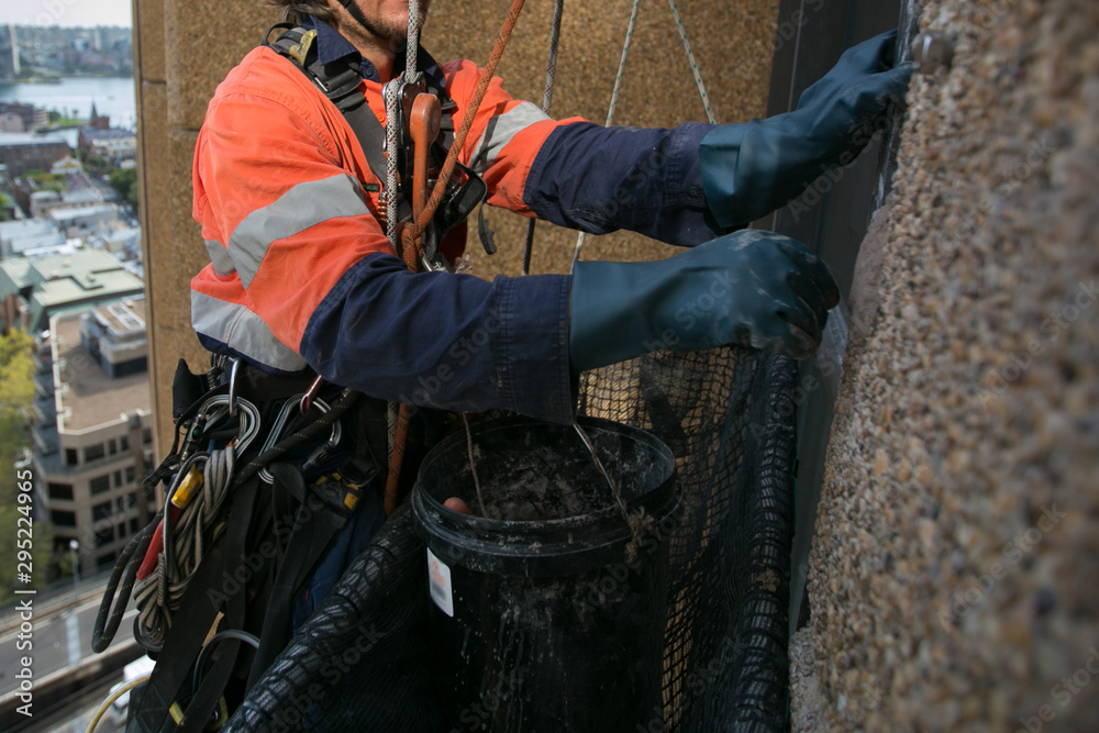 Close up pic of abseiler working at height abseiling twin nylon low stretch static rope wearing safety yellow helmet fall protection PPE harness using blue heavy duty glove conduct concrete repair Close up pic of abseiler working at height abseiling twin nylon low stretch static rope wearing safety yellow helmet fall protection PPE harness using blue heavy duty glove conduct concrete repair