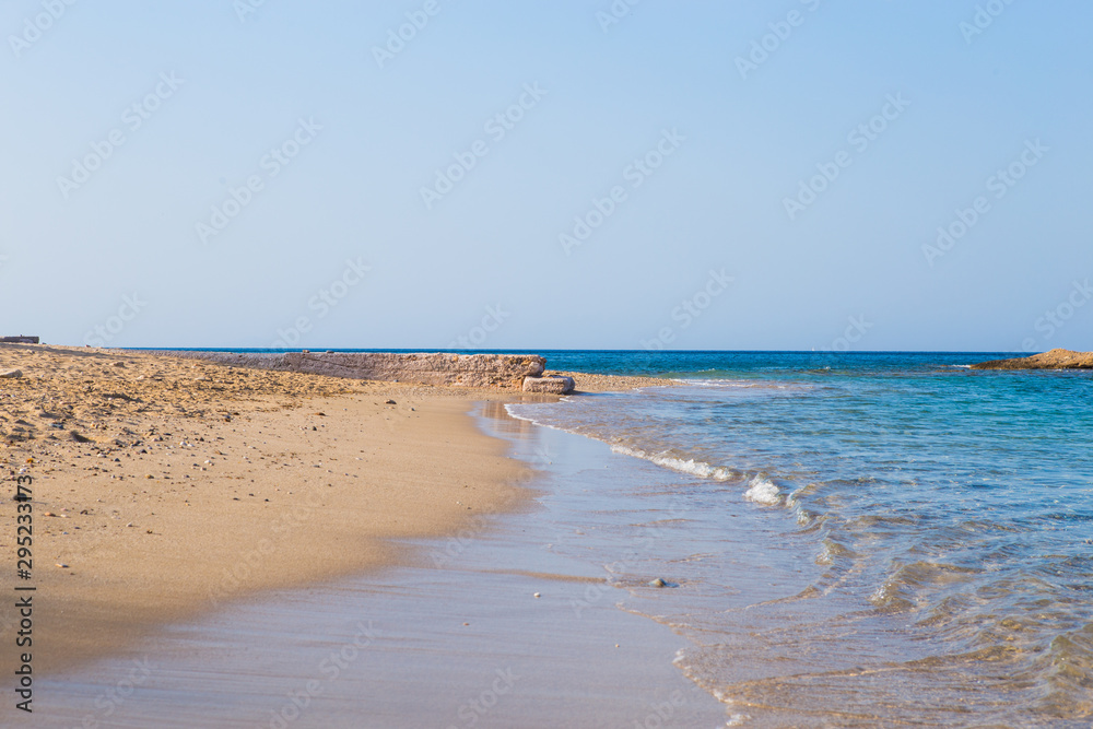 View of beautiful beach with clear blue water, golden sand, colorful boats and mountain on background. Summer landscape of Greece and Ionian Sea.